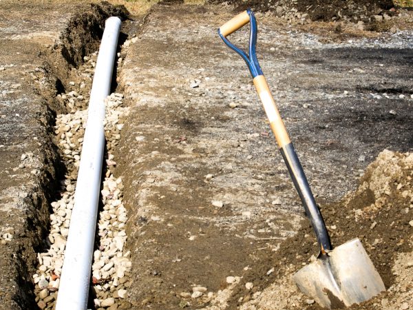 A shovel and pipe in the ground next to each other.