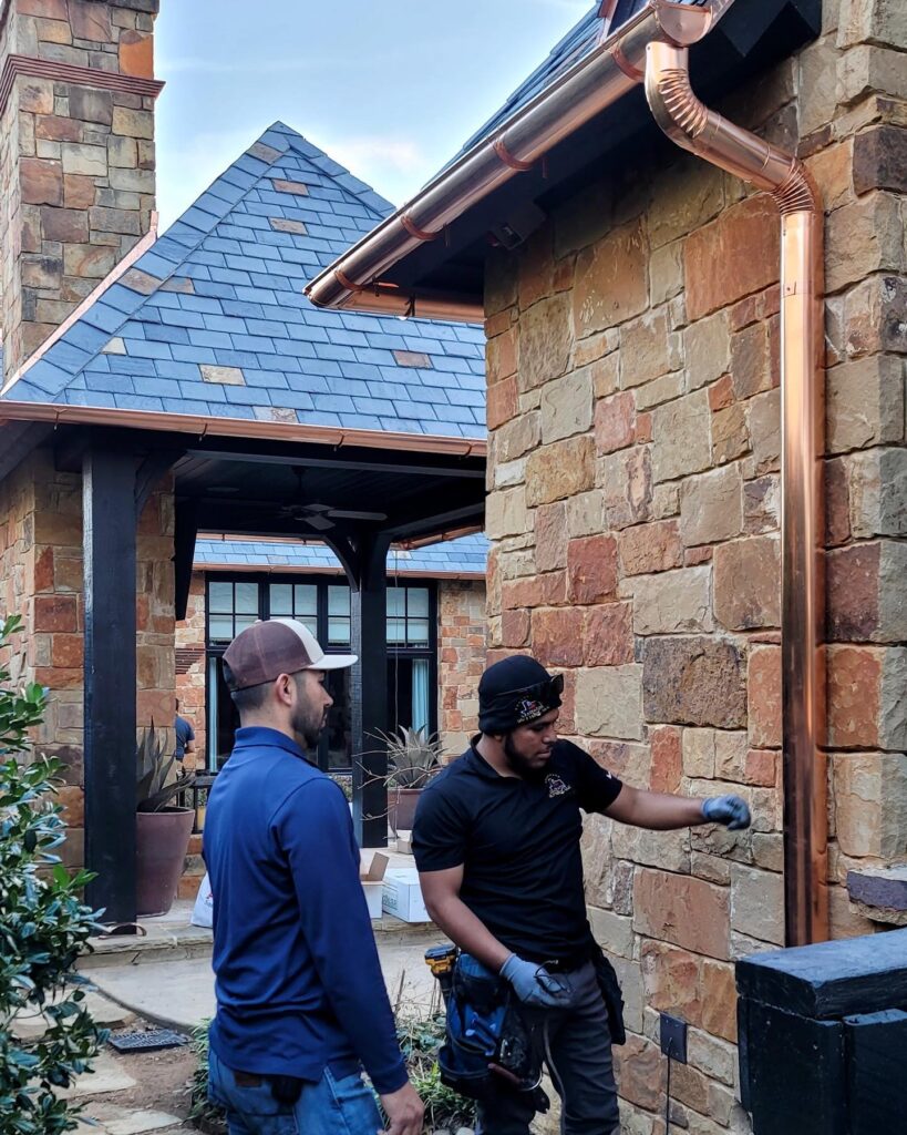 Two men standing next to a building with some kind of wood.