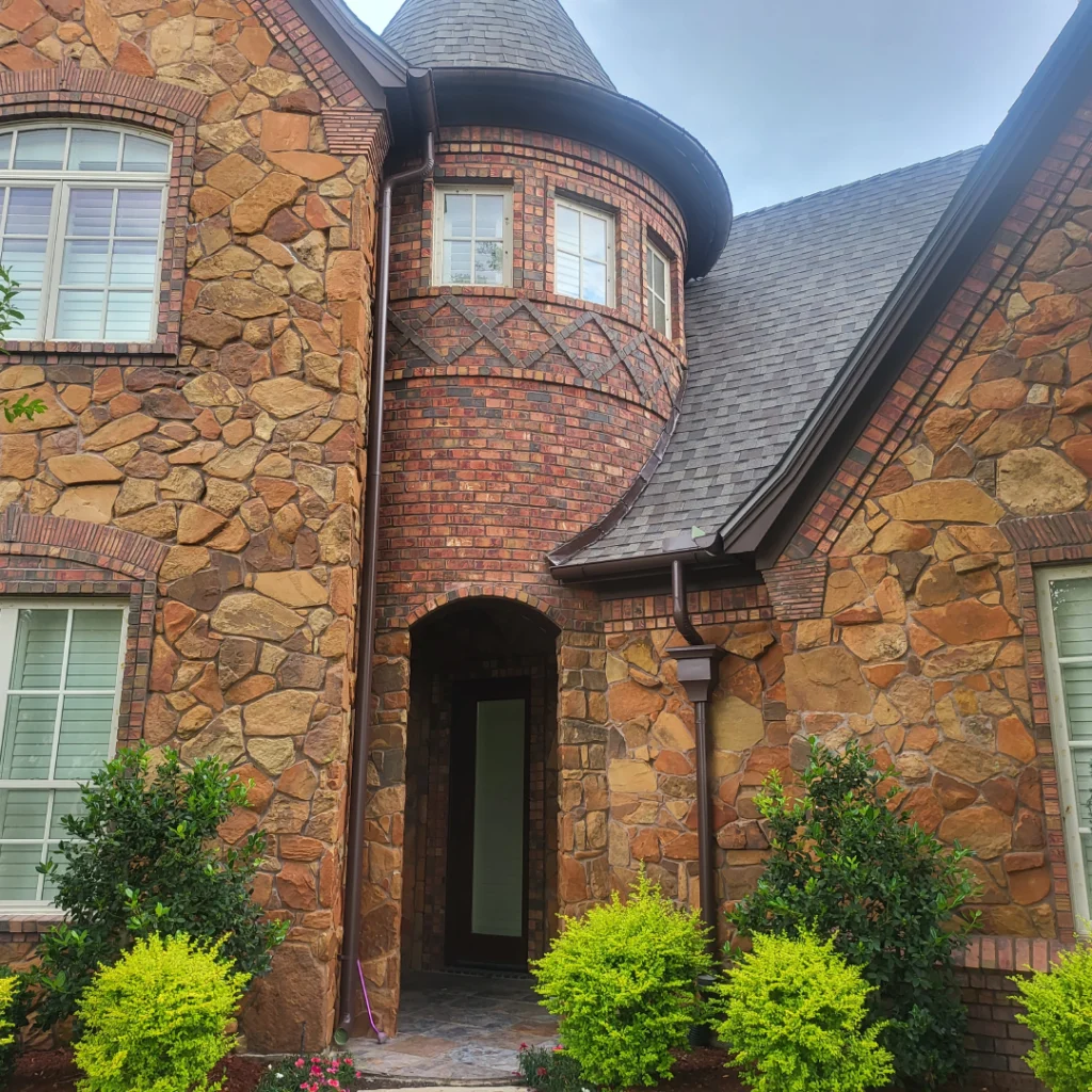 A large brick house with green bushes in front of it.